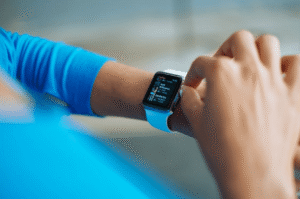 Pessoa de camisa azul consultando a tela de um smartwatch no pulso, exibindo informações de aplicativo.
